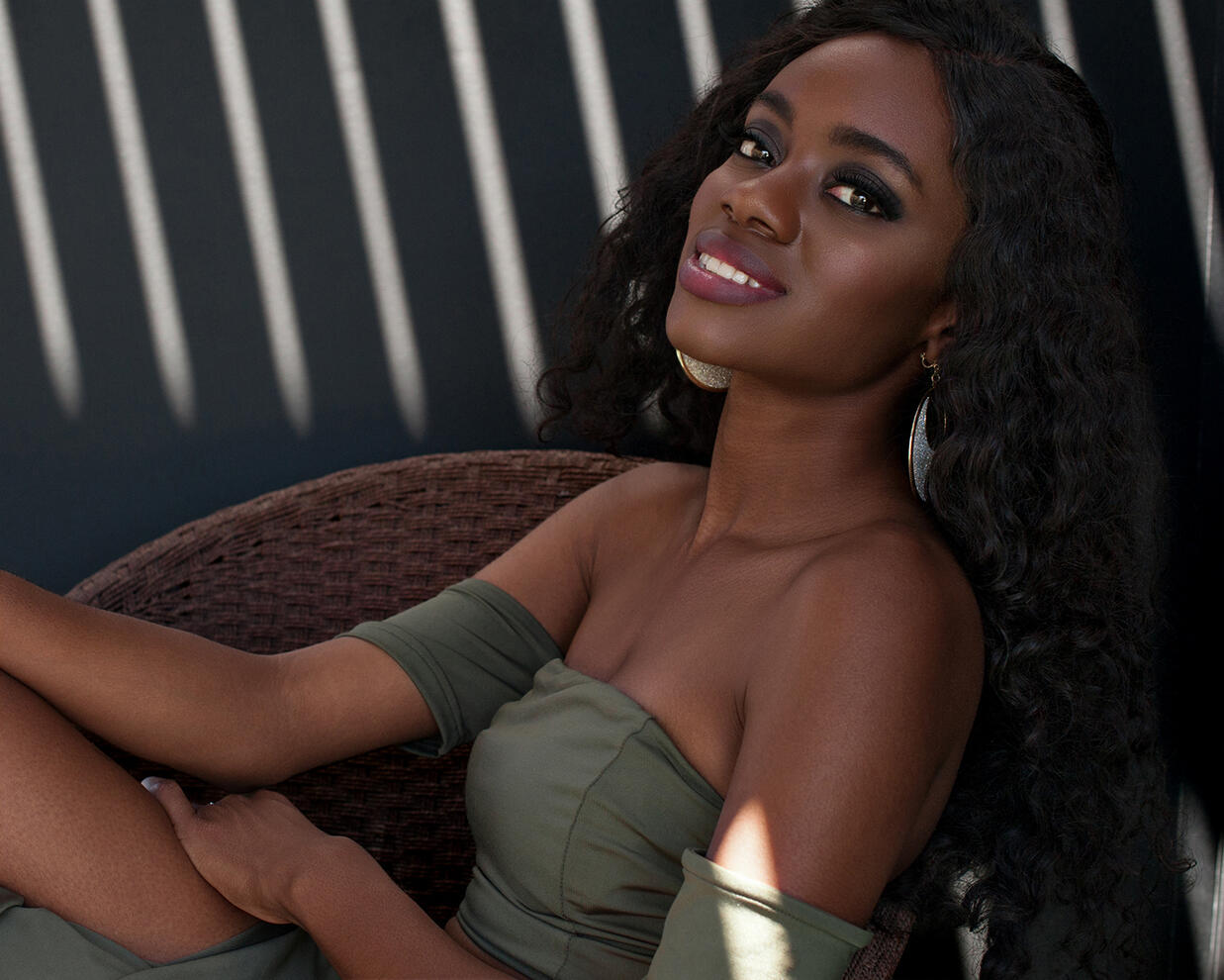 Personal Branding Black female model smiling reclining in a chair with shafts of sunlight behind by Tampa photographer Sidney Oster