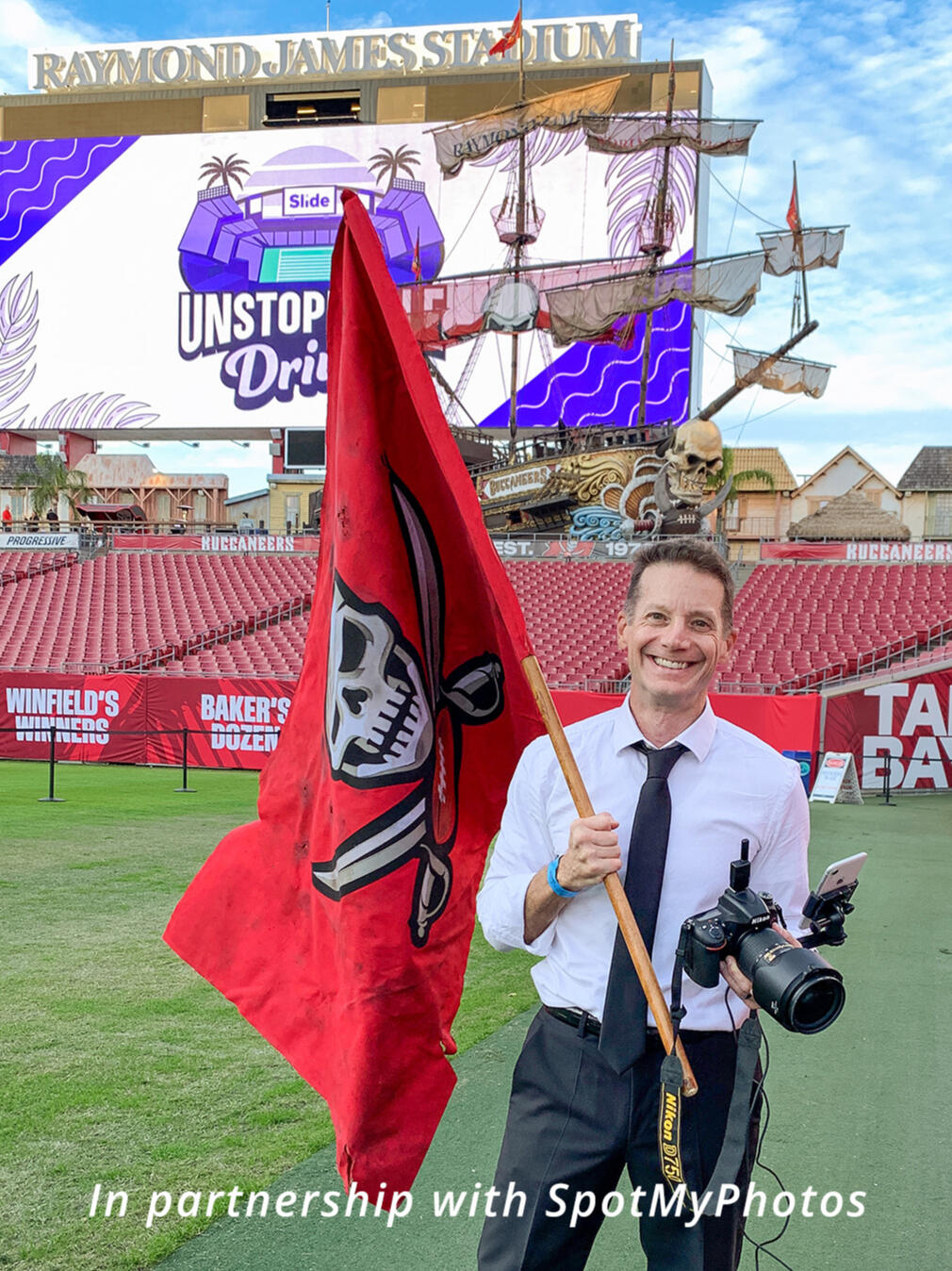Behind the Scenes ( BTS) at the Slide Insurance corporate holiday party Portrait of Sidney Oster holding a camera and the Tampa Bay Buccaneers flag on the field at Raymond James Stadium. In partnership with SpotMyPhotos.